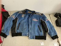 Front view of blue Ford Racing jacket showing patches, snap buttons, black panels, ribbed cuffs