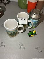 Pair of mugs, tin and die-cast tractor grouped
