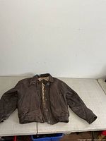 Front view of brown leather jacket laid flat