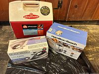 Igloo cooler, boxed Black+Decker iron and boxed Hamilton Beach toaster grouped together