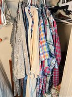 Rack showing approximately 10 assorted men's long-sleeve shirts in various plaid, solid and novelty patterns