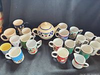 Group shot showing teapot centered, creamer, and approximately 18 Christmas mugs
