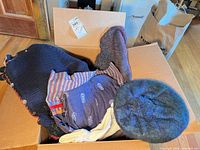 Open box showing pile of sweaters, scarves, beret