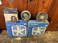 Group shot of two boxed Lasko fans, two Duracraft desk fans, one boxed Style Selections desk fan