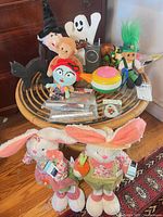 Overview of all toys on round wicker table, shows two large rabbit plush at front and assorted items on tabletop
