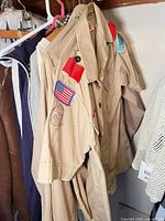 Boy Scouts tan uniform shirt with patches hanging among other garments