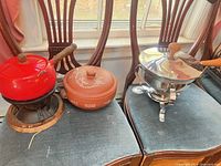 Three pots: red fondue on burner, terracotta casserole, stainless chafing dish on stand