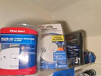 Shelf view showing First Alert alarm, Kidde combo alarm, boxed furniture kit and rolled towels