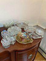 Multiple clear pressed glass pieces and one iridescent covered dish on wooden cabinet