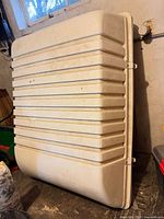 Off-white ribbed plastic rooftop cargo container housing standing on side