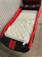 Top view of red and black race car bed frame with mattress for scale