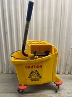 Side view of yellow rolling mop bucket showing wringer, handle, and casters