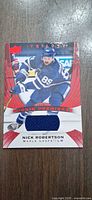 Front of Nick Robertson Trilogy Rookie Premieres jersey card showing player image, blue jersey swatch and serial number