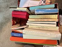 Stack of assorted boxed greeting card sets inside rose-patterned cardboard box