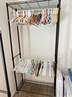Full view of black metal garment rack with mixed hangers on upper and lower chrome bars, wire shelves visible top and bottom