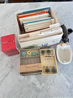 Lot overview showing greeting card organizer, TableTopics cube, two boxes of cocktail picks, ceramic dish, metal figurine