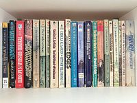 Row of 24 mass-market SF/F paperbacks on shelf, spines showing titles and authors