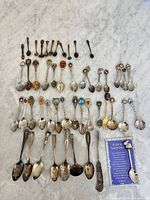 Full layout of all souvenir spoons and small forks on marble surface