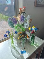 Group of four vases each containing colorful hand-blown glass flowers on a white surface