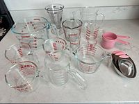 Full lot showing all glass measuring cups, plastic beaker, pink scoops, stainless scoops