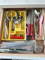 Drawer view showing majority of utensils including knives, cleaver, garlic press and tray of gadgets