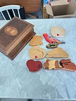 Group shot of veneered box and nine small wooden puzzles/puzzle boxes on tabletop