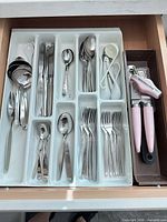 drawer view showing flatware, measuring sets, ladle, spoons, grater, pink KitchenAid can opener