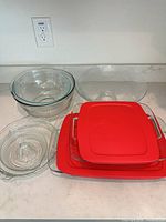 Group shot showing all glass items: two red-lidded Pyrex dishes, three nested mixing bowls, large serving bowl, citrus juicer