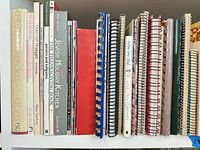 Row of cookbooks and spiral notebooks showing titles and bindings