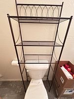 Front view of bronze metal over-the-toilet shelving unit showing three shelves and decorative top rail