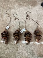 Four metal pinecone wind chimes laid out on carpet showing overall form and attached hooks
