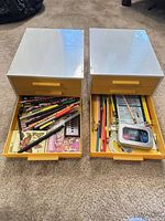 Two drawer units side by side with one drawer open on each showing pencils and stationery