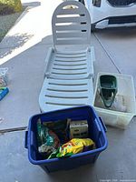 White molded plastic chaise lounge unfolded with blue and clear totes containing gardening supplies
