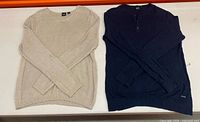 Beige and navy Hugo Boss sweaters laid flat