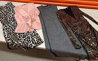 Four garments laid out: leopard dress, pink top, grey dress, sequin dress