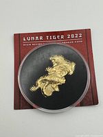 Front view of gold-plated tiger-shaped coin inside capsule on branded card