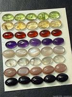 Front view of board showing rows of peridot, citrine, garnet, amethyst, moonstone, rose-toned stones, and black onyx cabochons