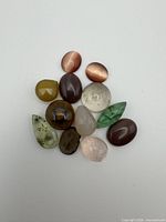 All twelve assorted polished semi-precious cabochon and faceted stones grouped on white background