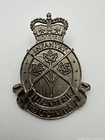 Front view of Canadian Infantry Corps cap badge with crown, bilingual text and Ducimus motto