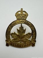 Front of brass cap badge showing maple leaf, crown, inscriptions