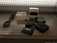 Three Apple TV units, Apple Remote in open box, power cable laid beside