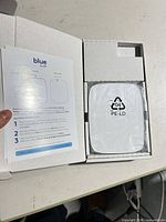 Opened box showing Blue by ADT Cellular Backup Bridge wrapped in plastic with instruction leaflet