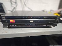 Front view of JVC multidisc DVD player showing brand badge, MP3 sticker, control buttons and display