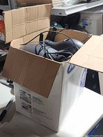 Open box showing black curved speakers, grey speaker, assorted cabling