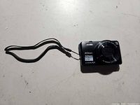 Front view showing Nikon Coolpix S7000 camera, lens markings, Wi-Fi and 20x zoom sticker, wrist strap