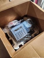 Postage meter in box with plastic wrap and Styrofoam supports