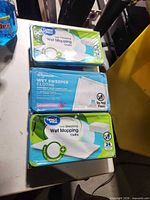 Three sealed tubs of wet mopping cloths (two Great Value, one Wegmans) top view