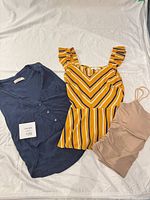 Three tops laid out: navy blouse, striped tank, beige camisole