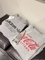 Adidas and Coca-Cola grey sweatshirts folded with silver Coke bottle