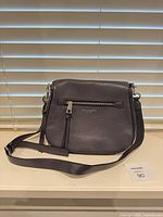 Front view of Marc Jacobs dark gray pebbled leather crossbody bag showing exterior zip pocket, tassel pull and adjustable strap